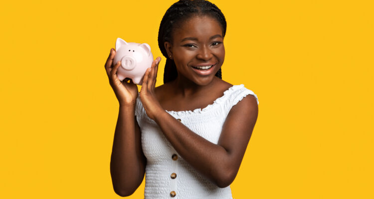 Money Savings. Cheerful black woman posing with piggy bank over yellow studio background, smart african lady enjoying economy, planning her budget and investments, smiling at camera, copy space