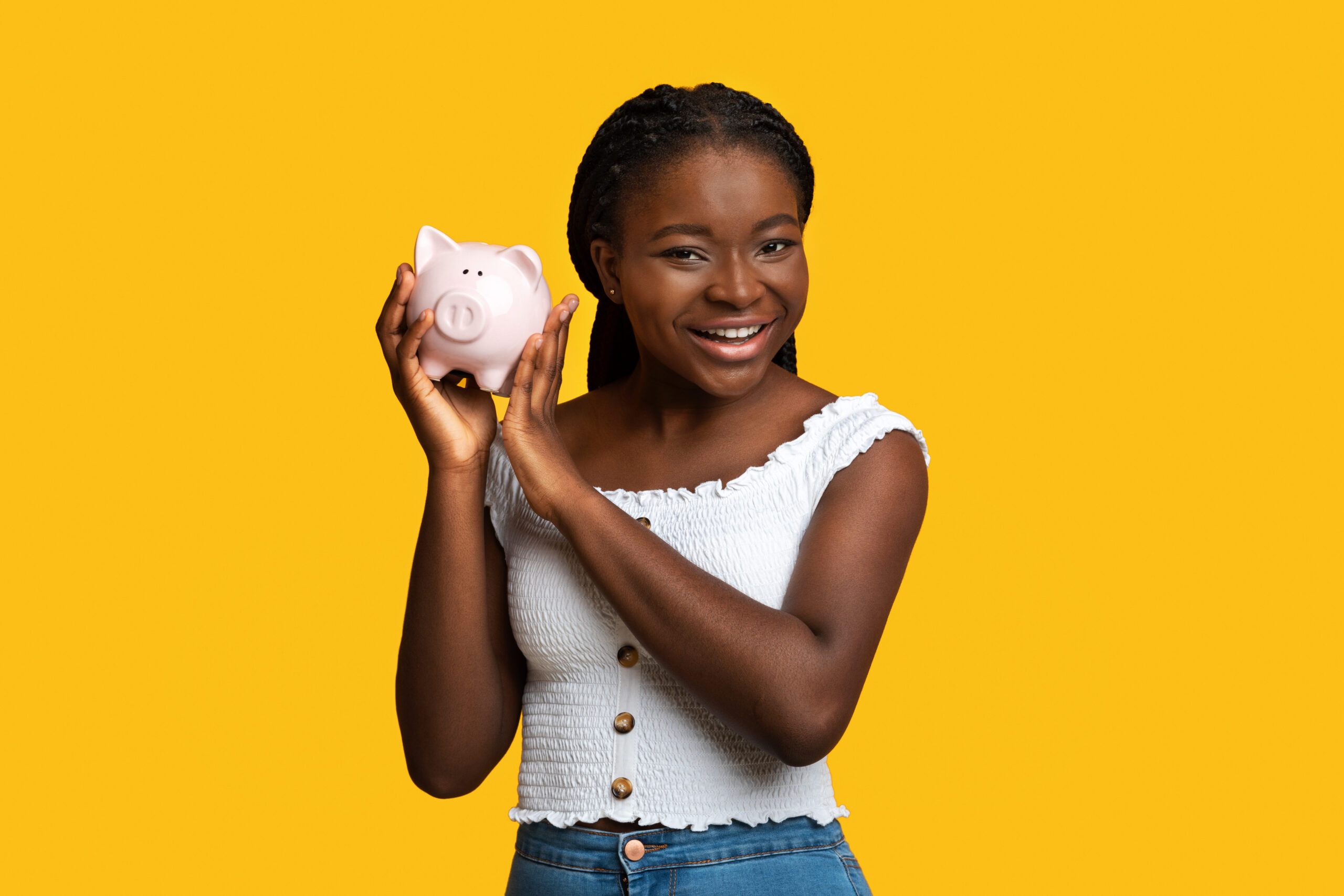 Money Savings. Cheerful black woman posing with piggy bank over yellow studio background, smart african lady enjoying economy, planning her budget and investments, smiling at camera, copy space