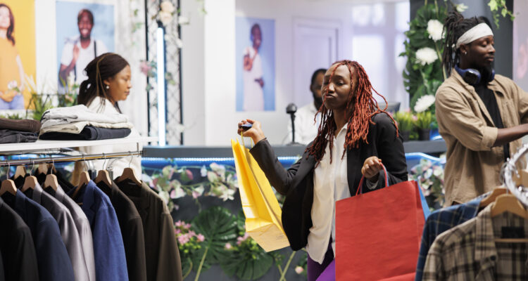 Customer carrying shopping bags and dancing in clothing store. Happy african american woman shopaholic buying new apparel with discount and holding packages in fashion boutique